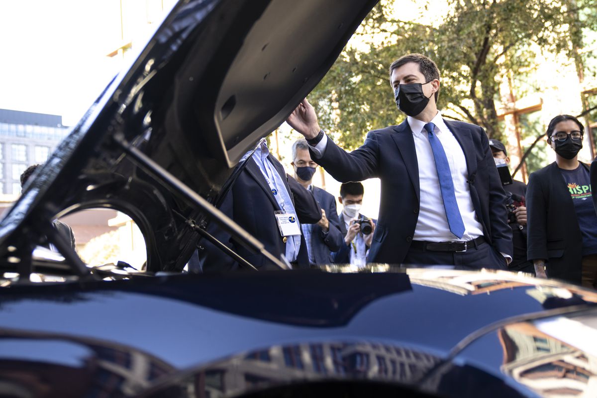 Secretary of Transportation Pete Buttigieg looking under the open hood of a Tesla car.