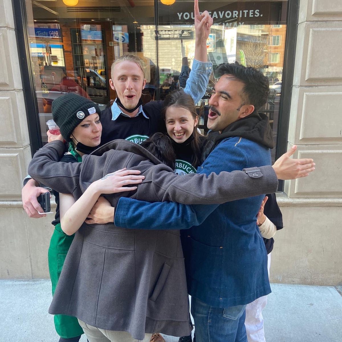 Starbucks workers and organizers in Queens stand on the sidewalk and hug in congratulations.