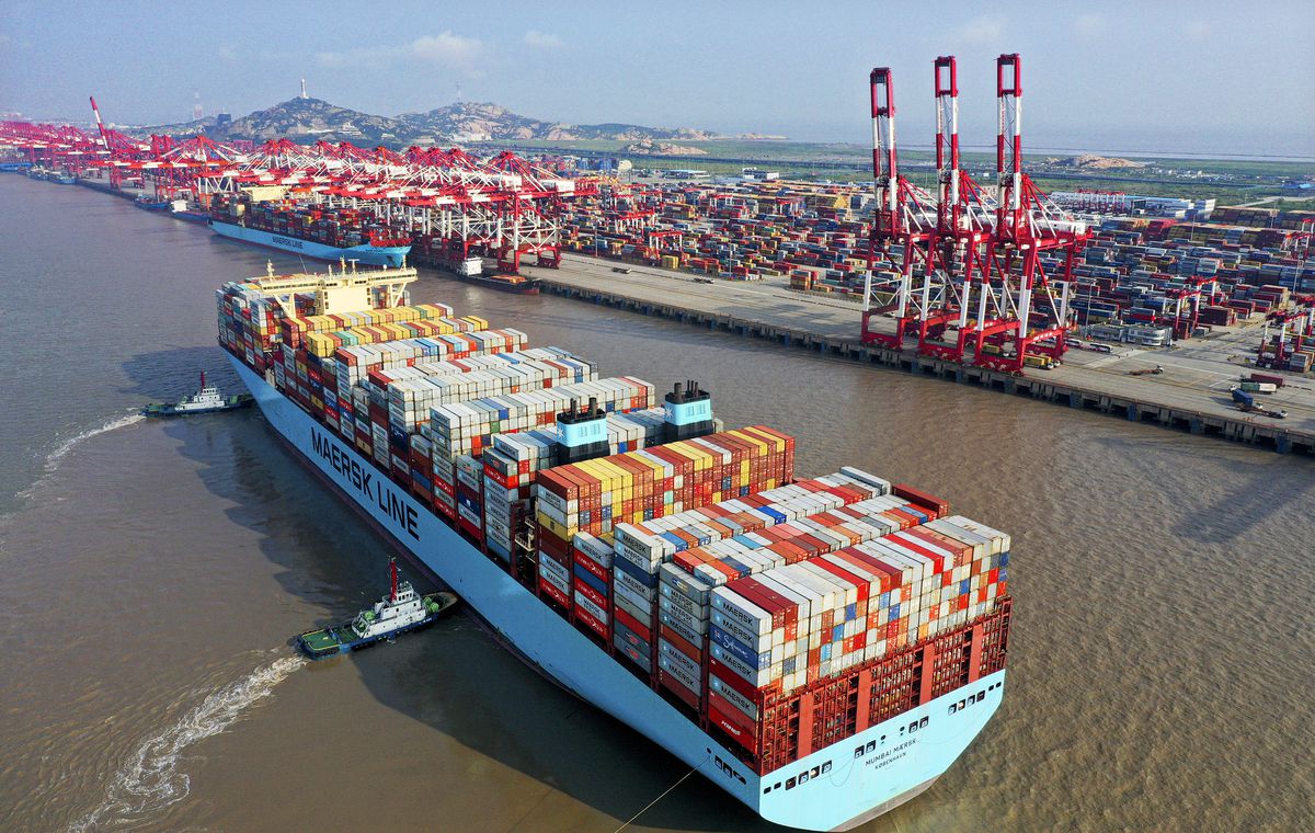 Two tugboats push a container ship sideways into its parking space at the loading dock.