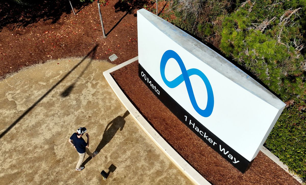 A person seen overhead walking past a large sign with the Meta logo.