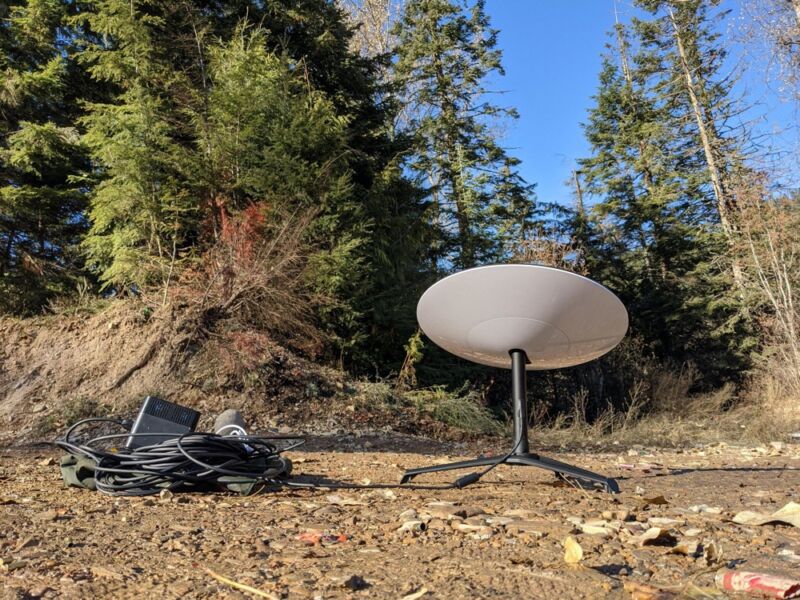 A satellite dish sitting in a forest next to a portable power supply.