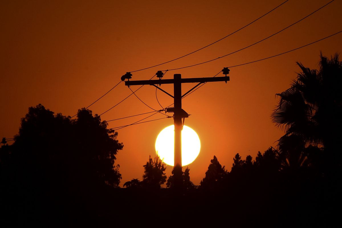 Power lines and trees silhouetted by the setting sun.