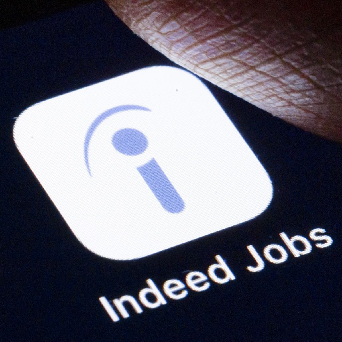 A finger hovering over the Indeed Jobs icon on a phone screen.