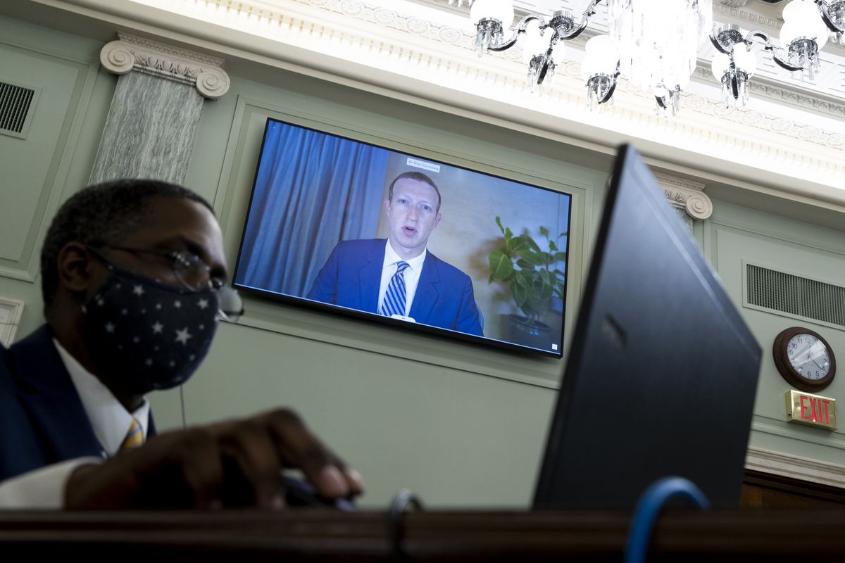 Mark Zuckerberg appears on a wall-mounted screen behind a staffer sitting at a computer.
