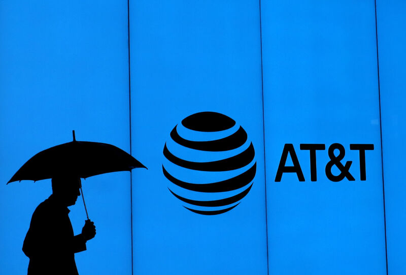 A man with an umbrella walking past a building with an AT&T logo.