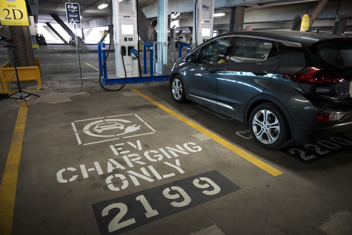 An electric vehicle charges in a parking garage next to a parking space reserved for EV charging.