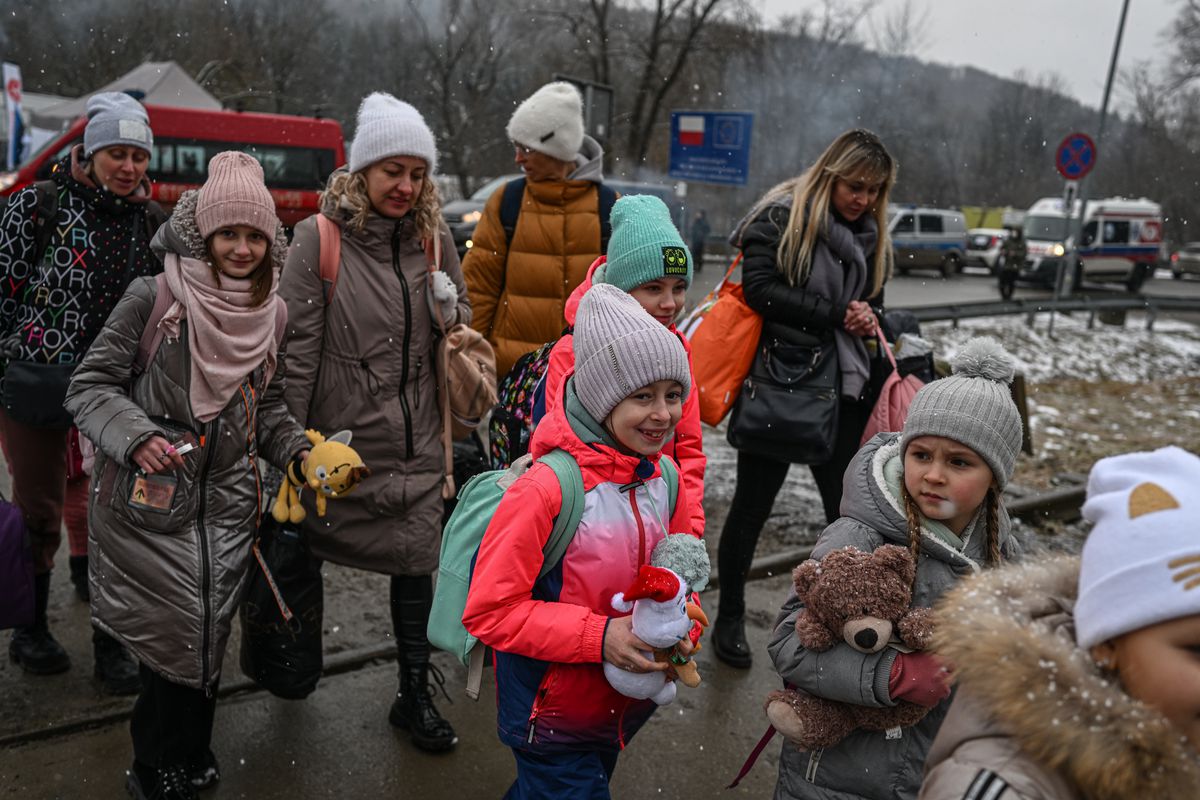 Ukrainian families with children walk across train tracks at the Polish border.