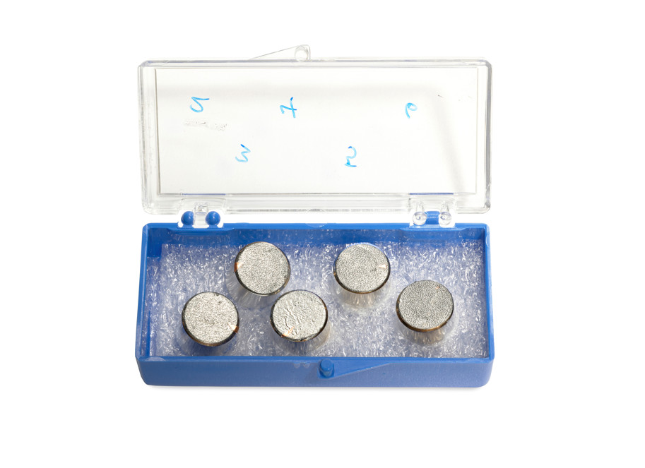 An open sample box containing five metal discs, each with moon dust stuck to it.