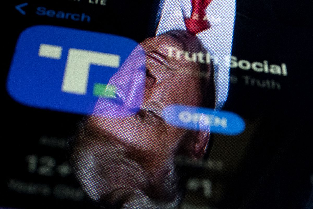 Donald Trump’s face reflects off a screen showing Truth Social’s logo.